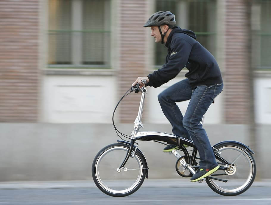 Seorang pria mengenakan helm sedang bersepeda dengan sepeda lipat di jalanan kota